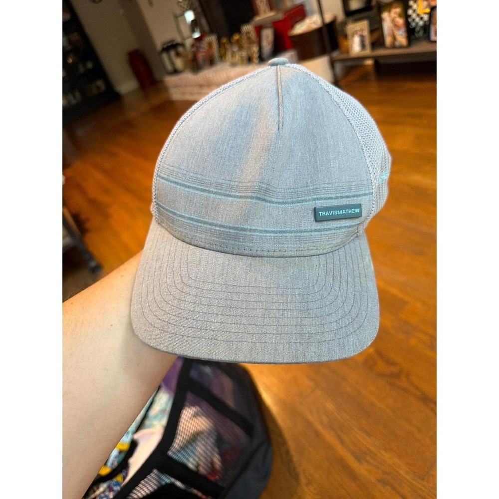 TravisMathew brand hat a gray color and striped detailing on the front